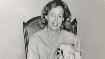 Smiling woman with wavy hair holding a fluffy dog, in a black and white photograph.