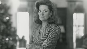Woman in a suit with arms crossed, standing confidently indoors.