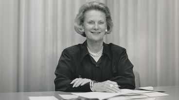 Smiling woman in a dark blouse sitting at a desk with papers.