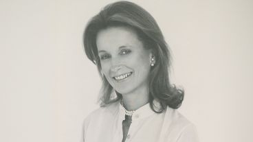 Smiling woman in black and white portrait, wearing pearls and a light shirt.