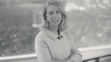 Woman smiling with arms crossed, wearing a light-colored jacket. Black and white photo.
