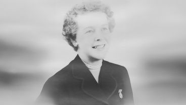 Smiling woman in a suit with pearls, in black and white.