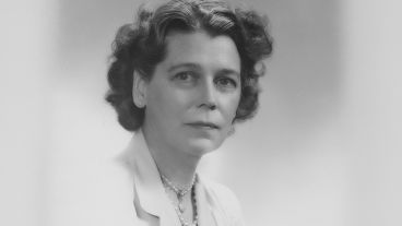 Black and white portrait of a woman in a blazer, with curled hair and a serious expression.