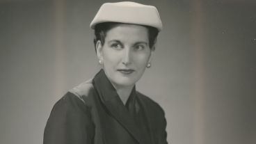 Woman in a suit and white hat, wearing pearl earrings, in a vintage black-and-white photo.