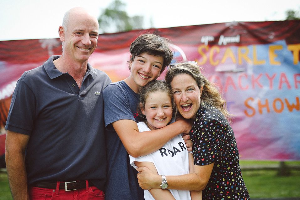 A family with a mom, dad, son, and daughter smiles while hugging. 