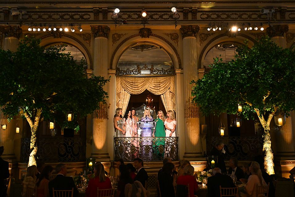Six people standing on a balcony, one of whom is speaking from a podium addressing attendees of the Spring Ball.