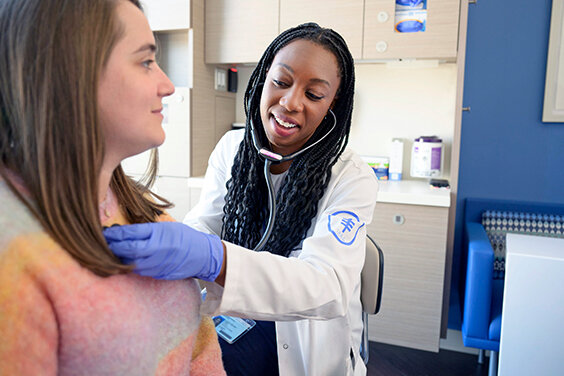 An MSK clinician smiles as she holds a stethoscope to a patient’s chest. 