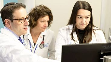 Three MSK blood cancer specialists look at a computer monitor.
