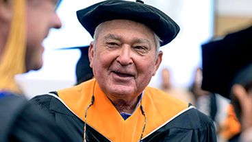 Louis V. Gerstner, Jr. smiles, wearing a cap and gown. 