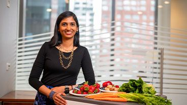 Dr. Urvi Shah standing behind a table full of fresh fruits and vegetables. 